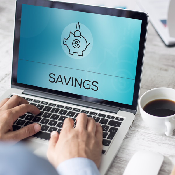 Hands rest on a laptop keyboard with the word "Savings" on the screen and an icon of a piggy bank